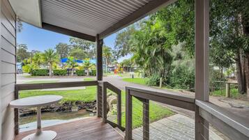 A covered outdoor area with a table and a view of a park with trees and playground equipment.