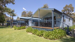 A row of blue cabins with a covered porch, surrounded by well-maintained grass and plants.