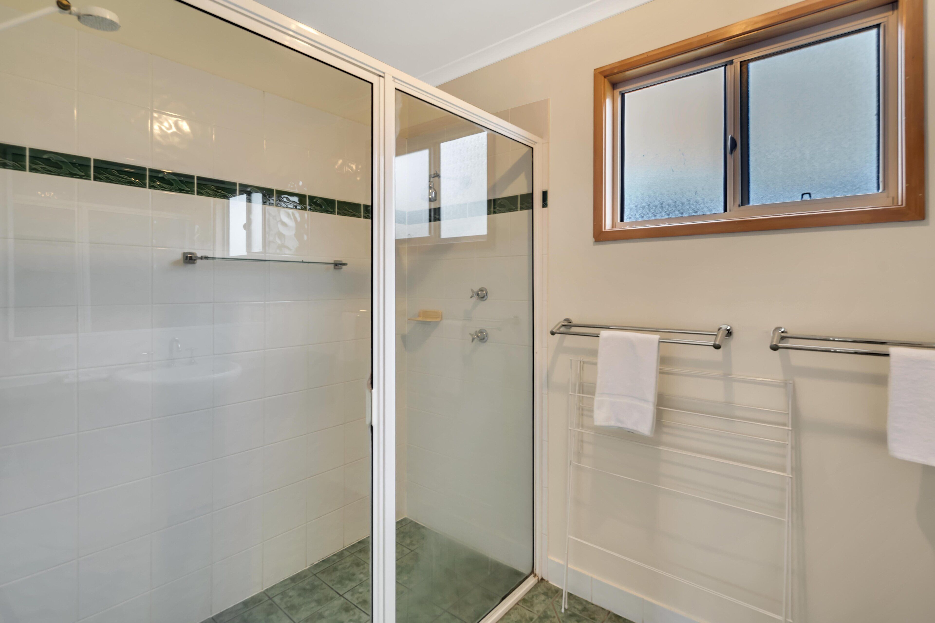 A bathroom with a glass shower enclosure, a sink, and a towel rack.
