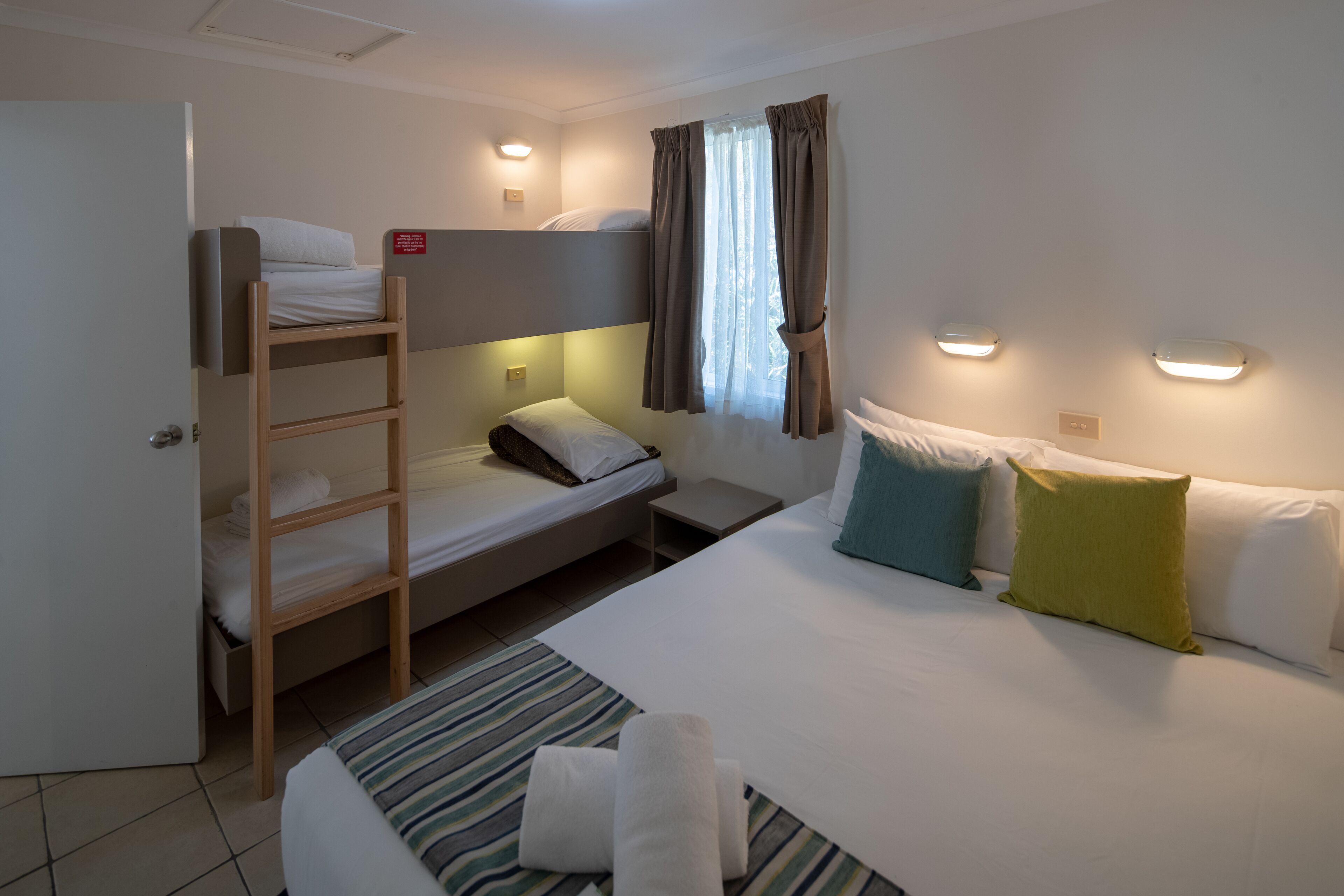 A room with a bunk bed, a desk, and a bed with pillows.