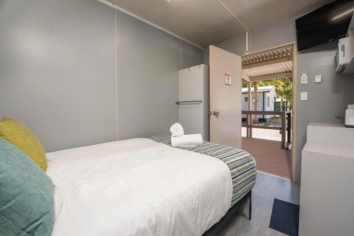 Hotelkamer met een bed, een klein tafeltje, een stoel, een garderobe en een deur naar een buitenruimte.