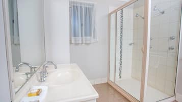 A bathroom with a double sink, a glass shower enclosure, and a window with sheer curtains.