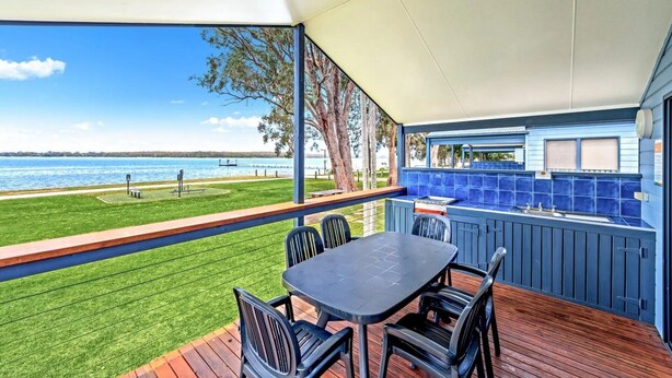A covered outdoor area with a table and chairs, a barbecue station, and a view of the water.