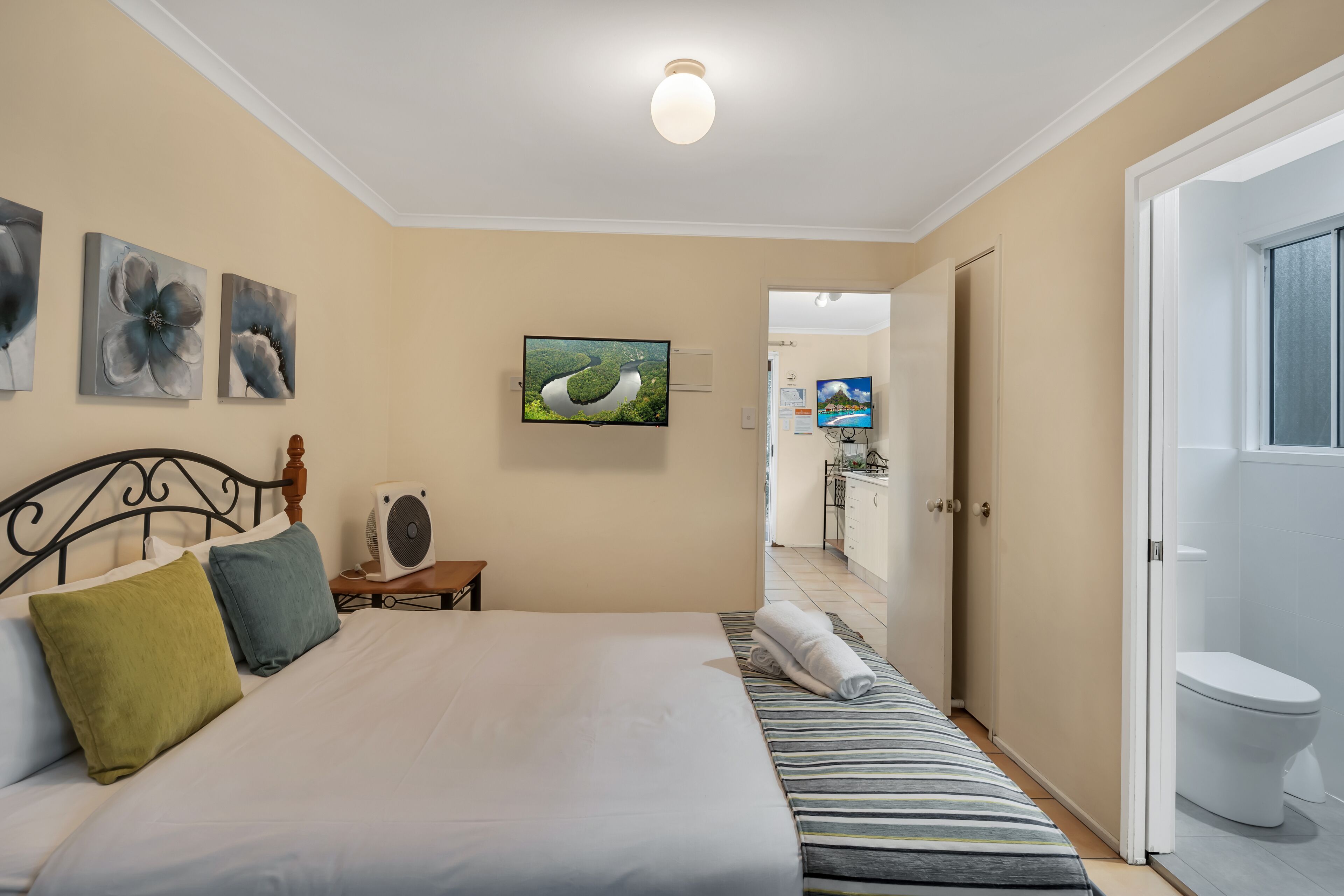 Quarto com cama, almofadas, televisão e porta para um banheiro.