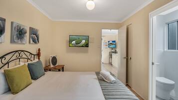 Quarto com cama, almofadas, televisão e porta para um banheiro.