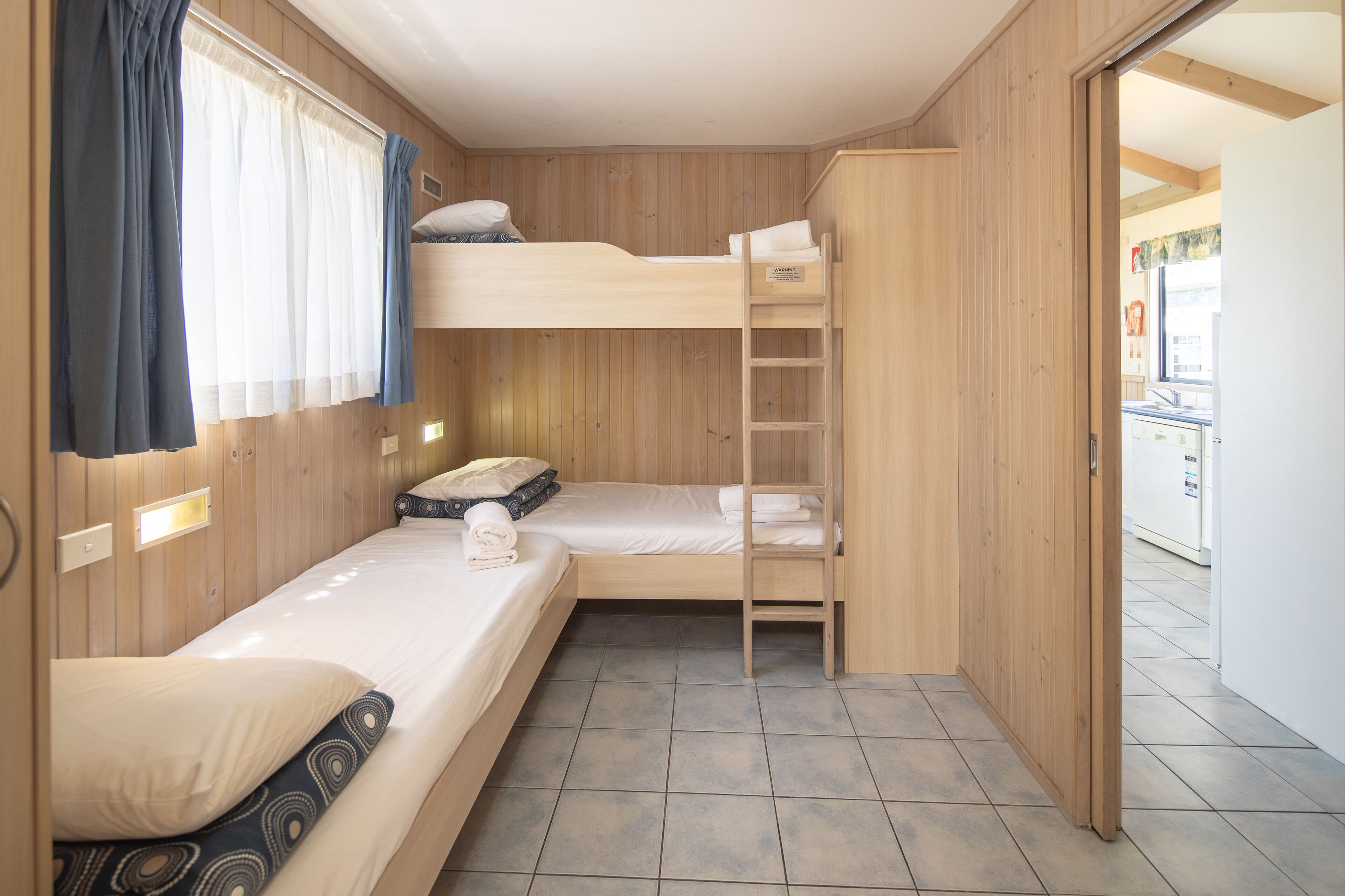 A compact room with a bunk bed, a small desk, and a window with curtains.