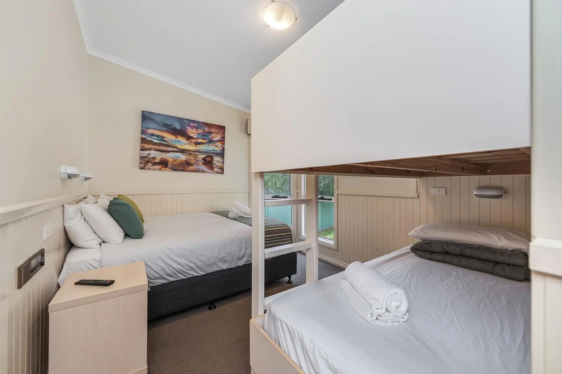 A room with two beds, a painting on the wall, and a window providing a view.