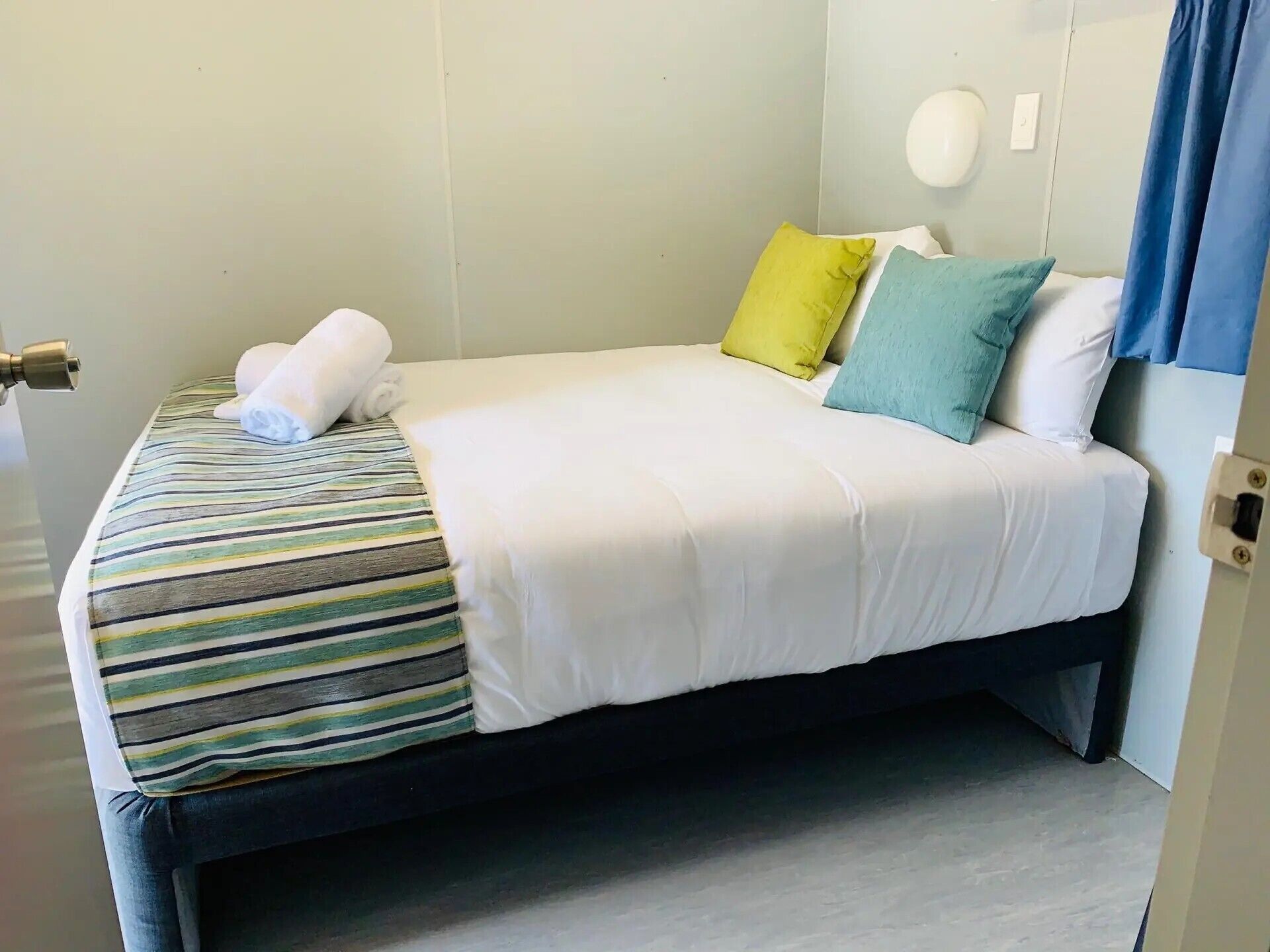 Una cama bien hecha con una colcha a rayas y almohadas en tonos amarillo y azul.