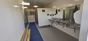 A narrow corridor with a blue carpet leading to a bathroom with multiple sinks and a mirror. - Waitomo Top 10 Holiday Park (Waitomo Caves)