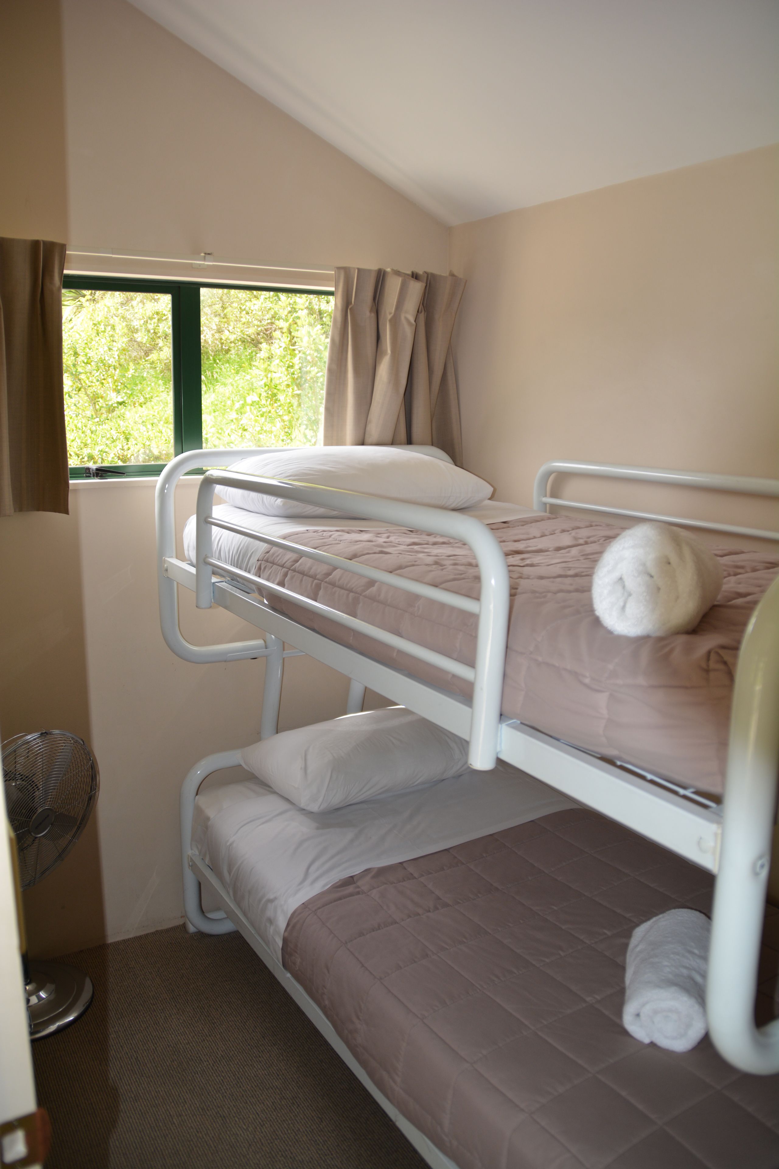 A bunk bed room with a window, curtains, and a fan.