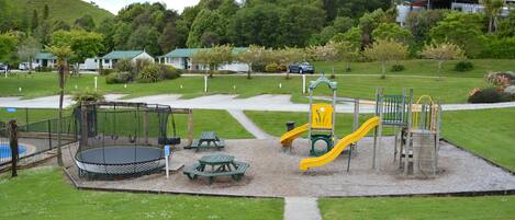 A playground with a swing set, slide, and picnic tables.