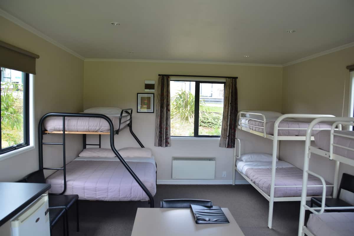 A dormitory room with bunk beds, a desk, and a radiator.
