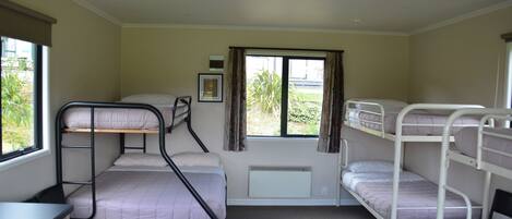 A dormitory room with bunk beds, a desk, and a radiator.