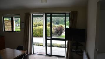 A room with a sliding glass door leading to a garden, a television, and a dining area with chairs.