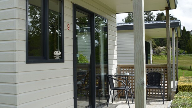 Une maison moderne dotée d’un porche abrité, d’une plaque portant le numéro « 9 », et d’un petit espace extérieur aménagé avec des chaises et une table.