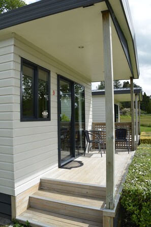 A modern house with a covered porch, a number '9' sign, and a small outdoor seating area with chairs and a table. - Waitomo Top 10 Holiday Park (Waitomo Caves)