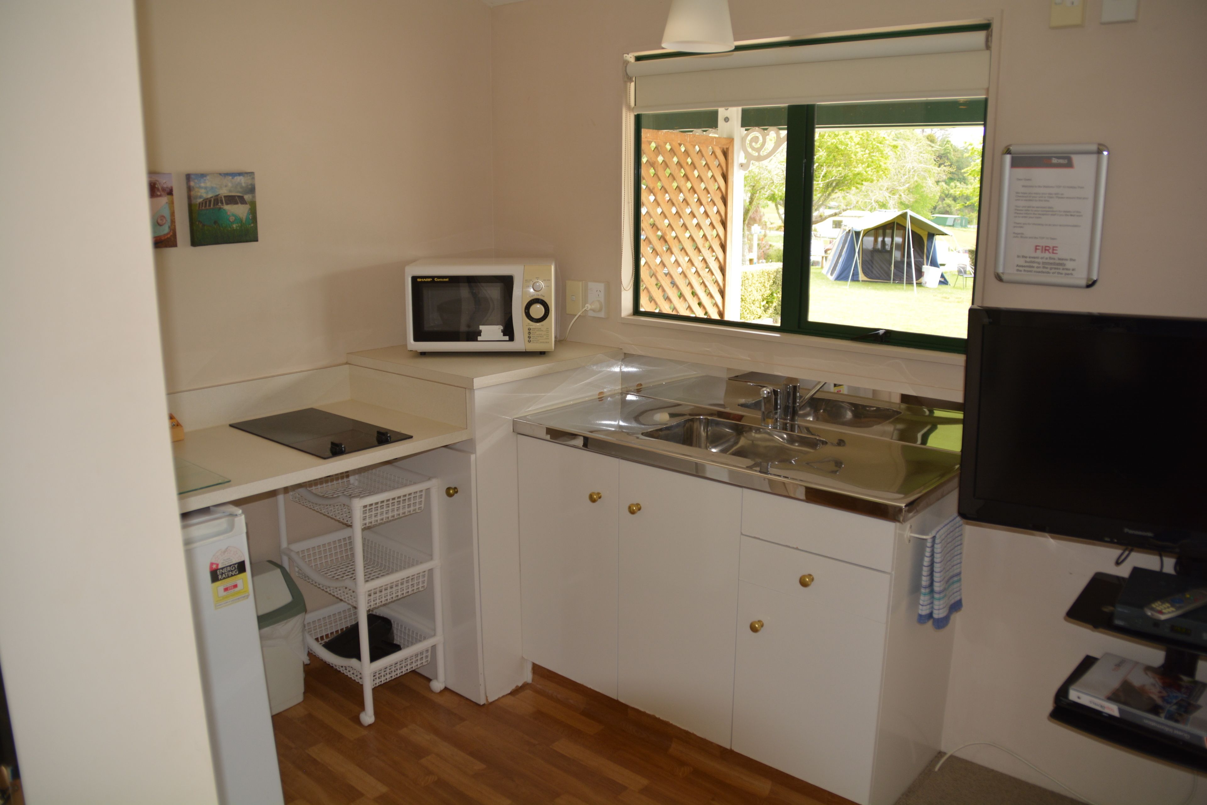 A compact kitchen with white cabinets, a microwave, a sink, and a window with a view of the outdoors.
