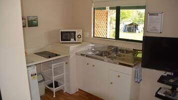 A compact kitchen with white cabinets, a microwave, a sink, and a window with a view of the outdoors.