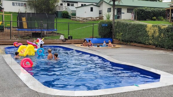 A swimming pool with inflatable toys and a fenced area with a play structure. - Waitomo Top 10 Holiday Park (Waitomo Caves)