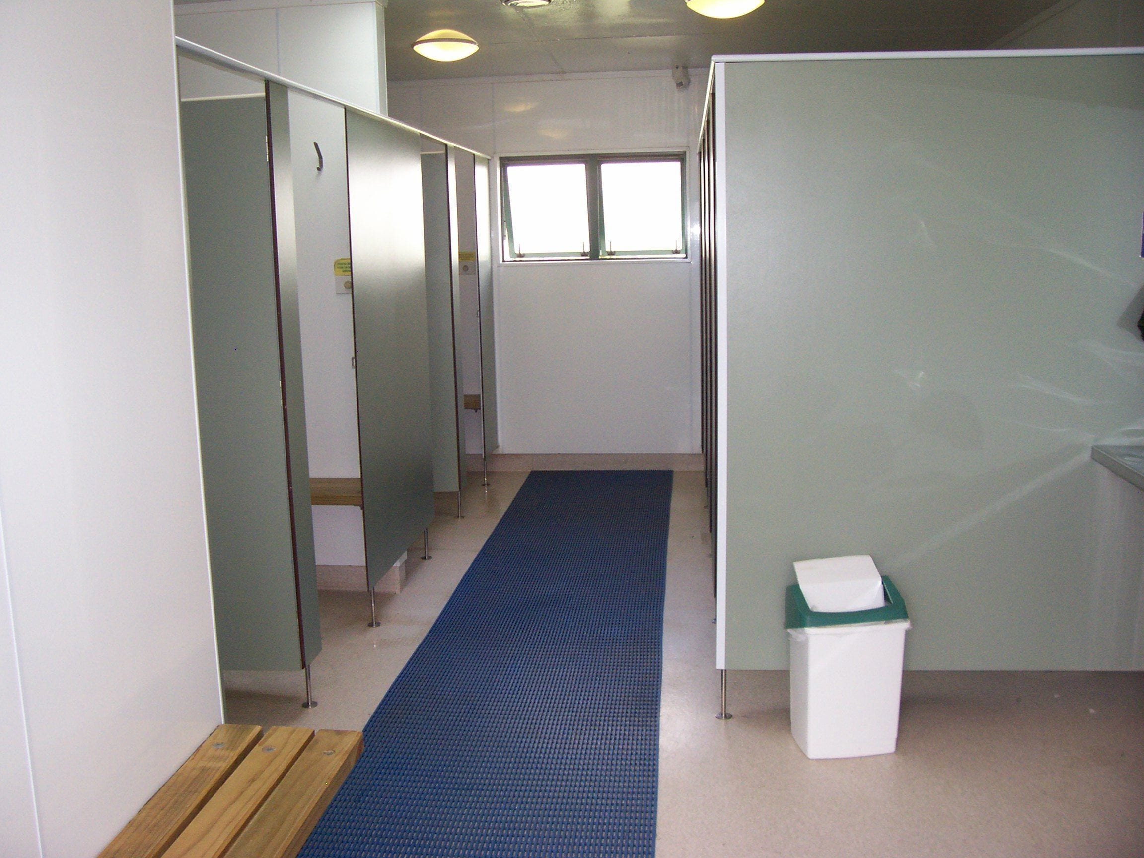 A corridor with a blue carpet, partitioned rooms, a window, and a trash bin.