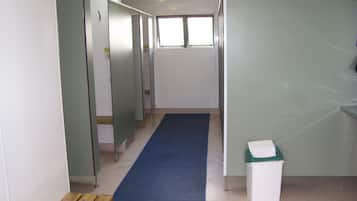 A corridor with a blue carpet, partitioned rooms, a window, and a trash bin.
