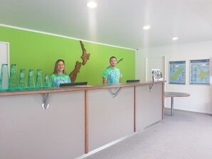 A reception desk with two staff members, a green wall, and two maps on the wall. - Waitomo Top 10 Holiday Park (Waitomo Caves)