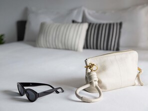 A bed with white bedding, a white pillow, a striped pillow, and a white handbag with a gold clasp. - Coffs Harbour Budget Stay (Coffs Harbour)
