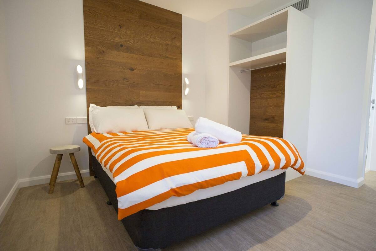 A bed with a striped blanket, a small stool, and a wooden headboard.