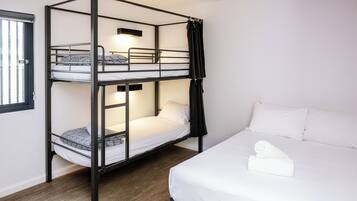 Habitación con literas, una cama individual y una toalla bien doblada en la litera inferior.