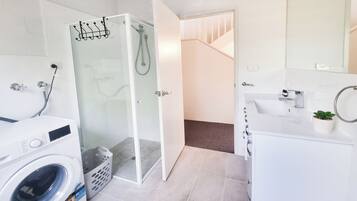 A modern bathroom with a glass shower enclosure, a washing machine, a sink, and a small potted plant.