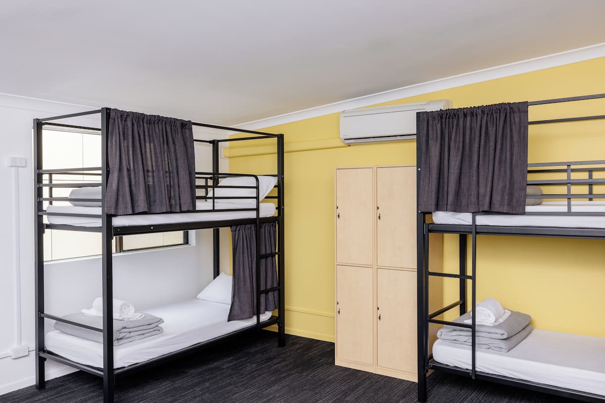 Two bunk beds with curtains, a wardrobe, and an air conditioning unit in a room with yellow walls.