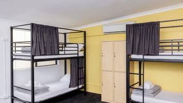 Dos literas con cortinas, un armario y un equipo de aire acondicionado en una habitación con paredes amarillas.