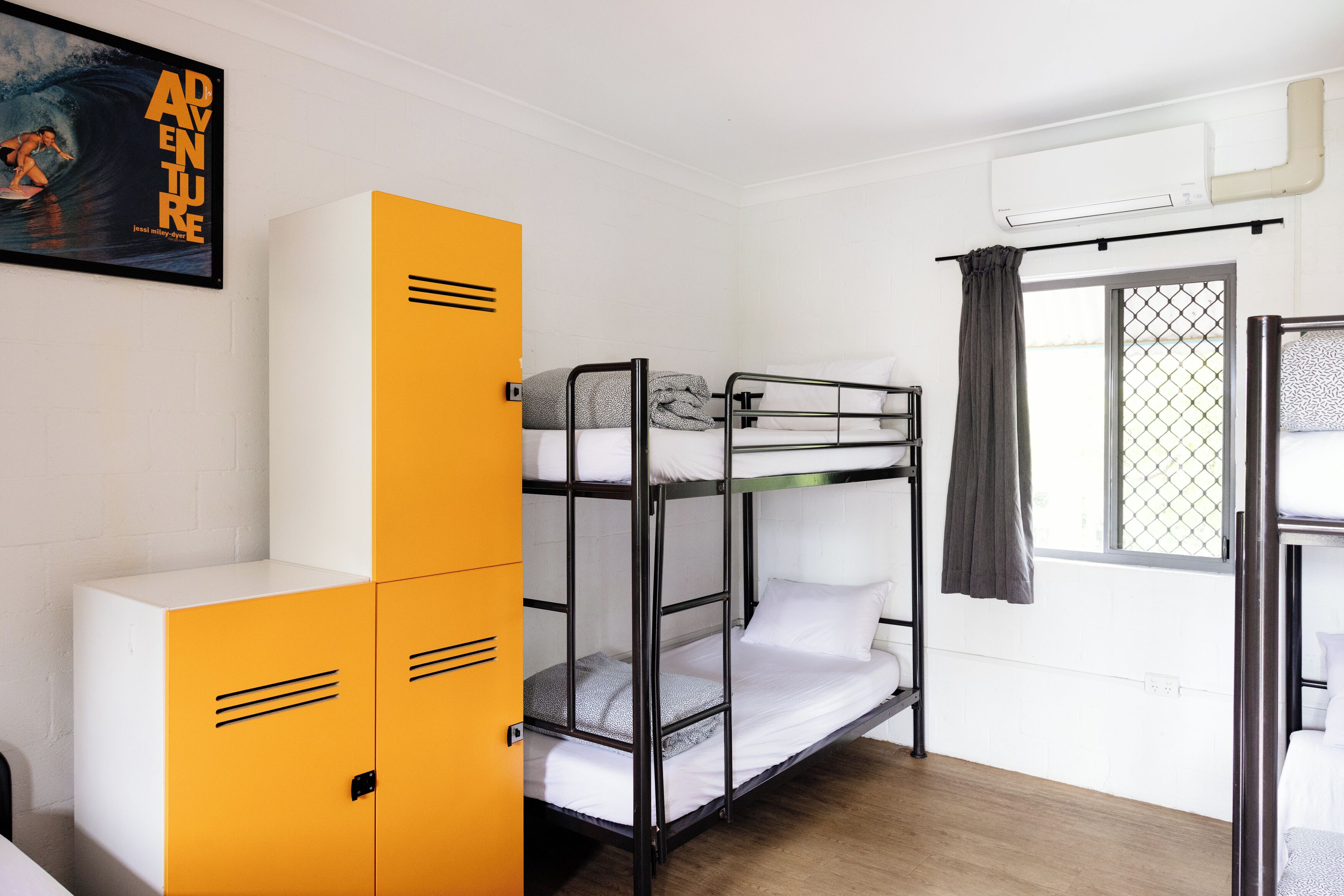 A bunk bed room with a white wall, a yellow cabinet, and a window with a curtain.