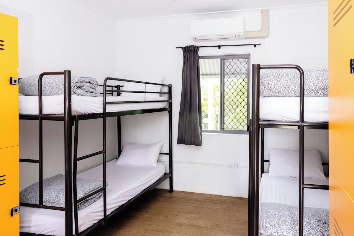 A dormitory room with bunk beds, a window with a curtain, and an air conditioning unit on the wall.