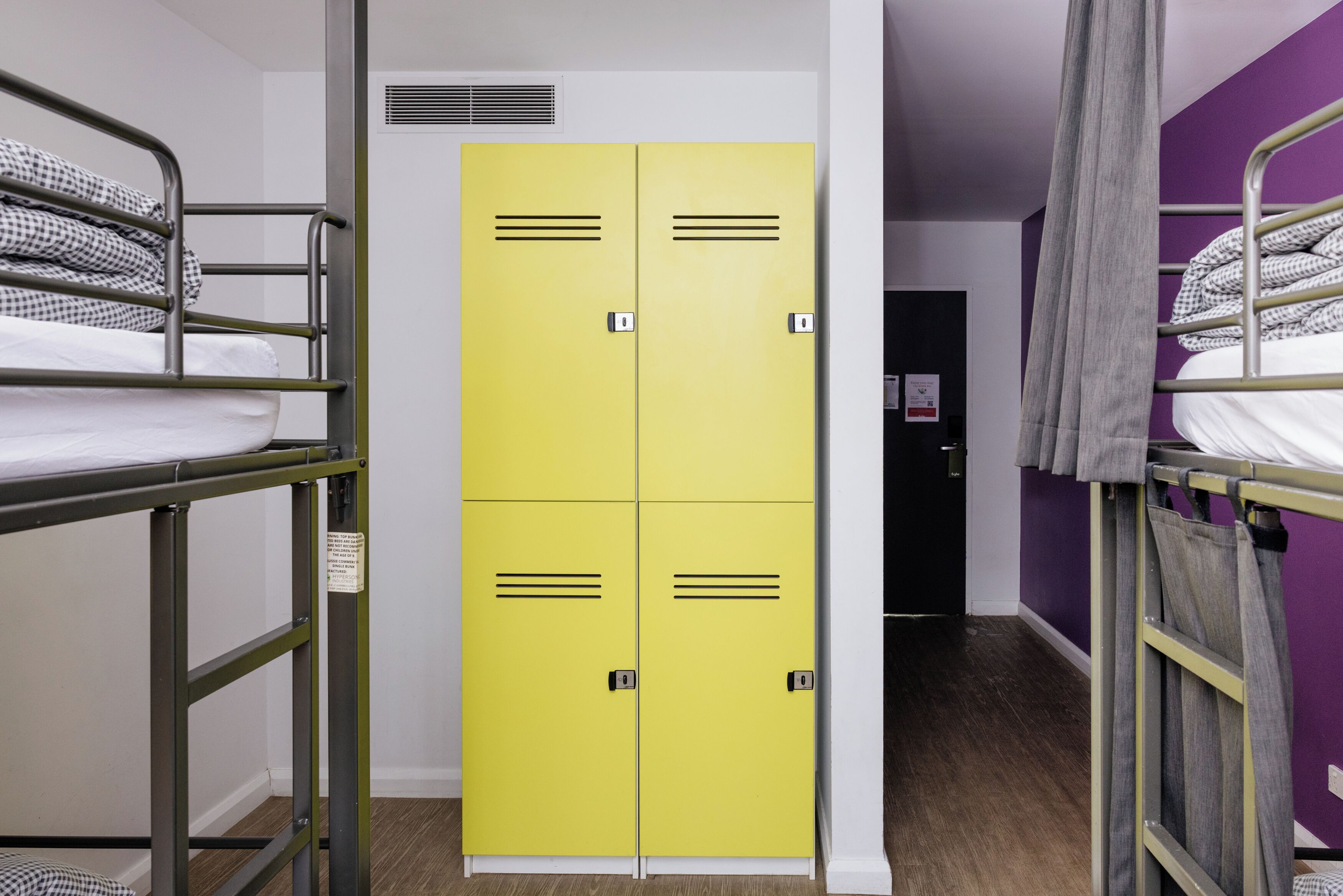 A dormitory room with bunk beds, a yellow wardrobe, and a door with a sign.