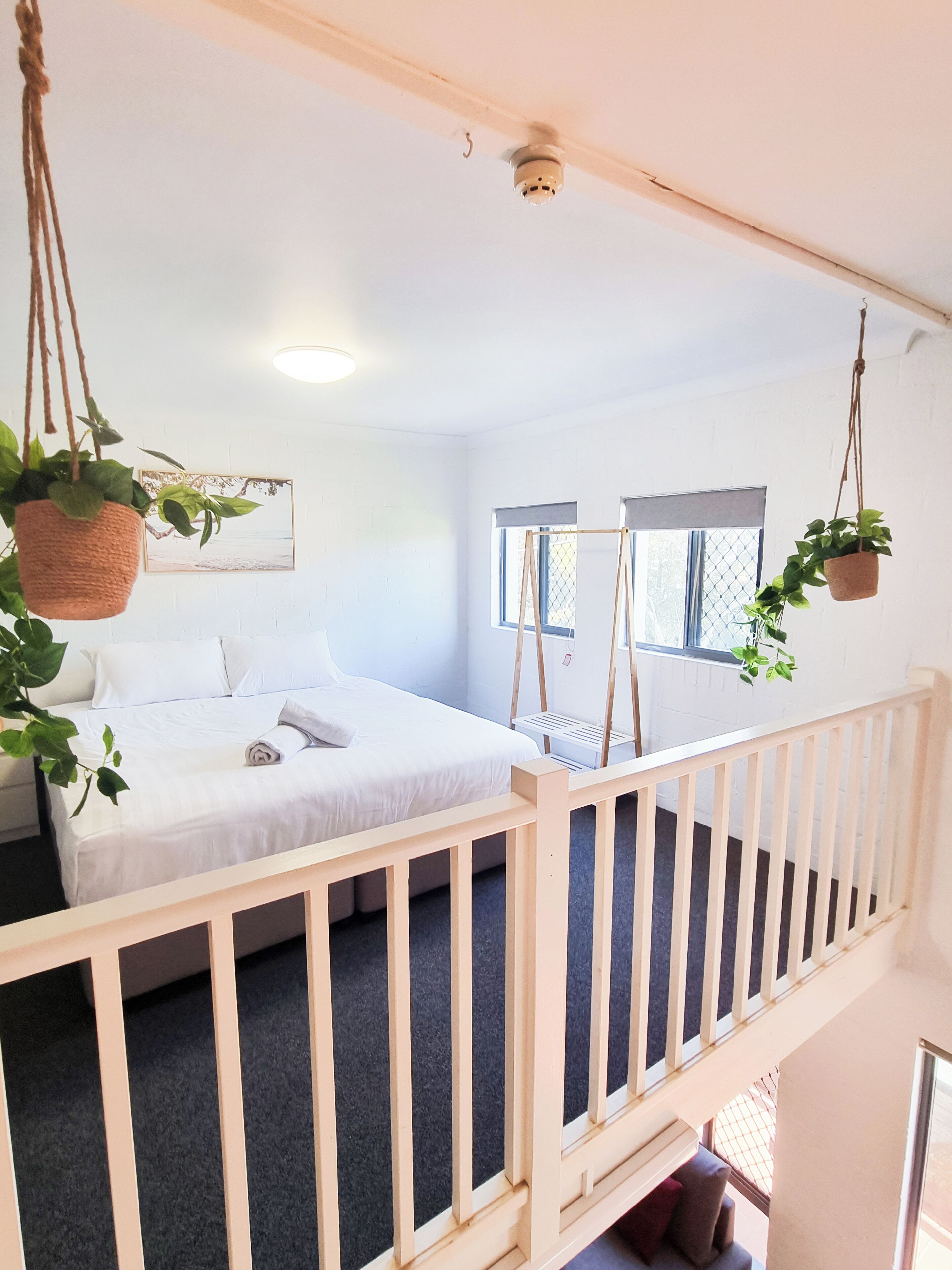 A bedroom with a bed, a hanging plant, a window, and a staircase.