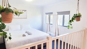 A bedroom with a bed, a hanging plant, a window, and a staircase.