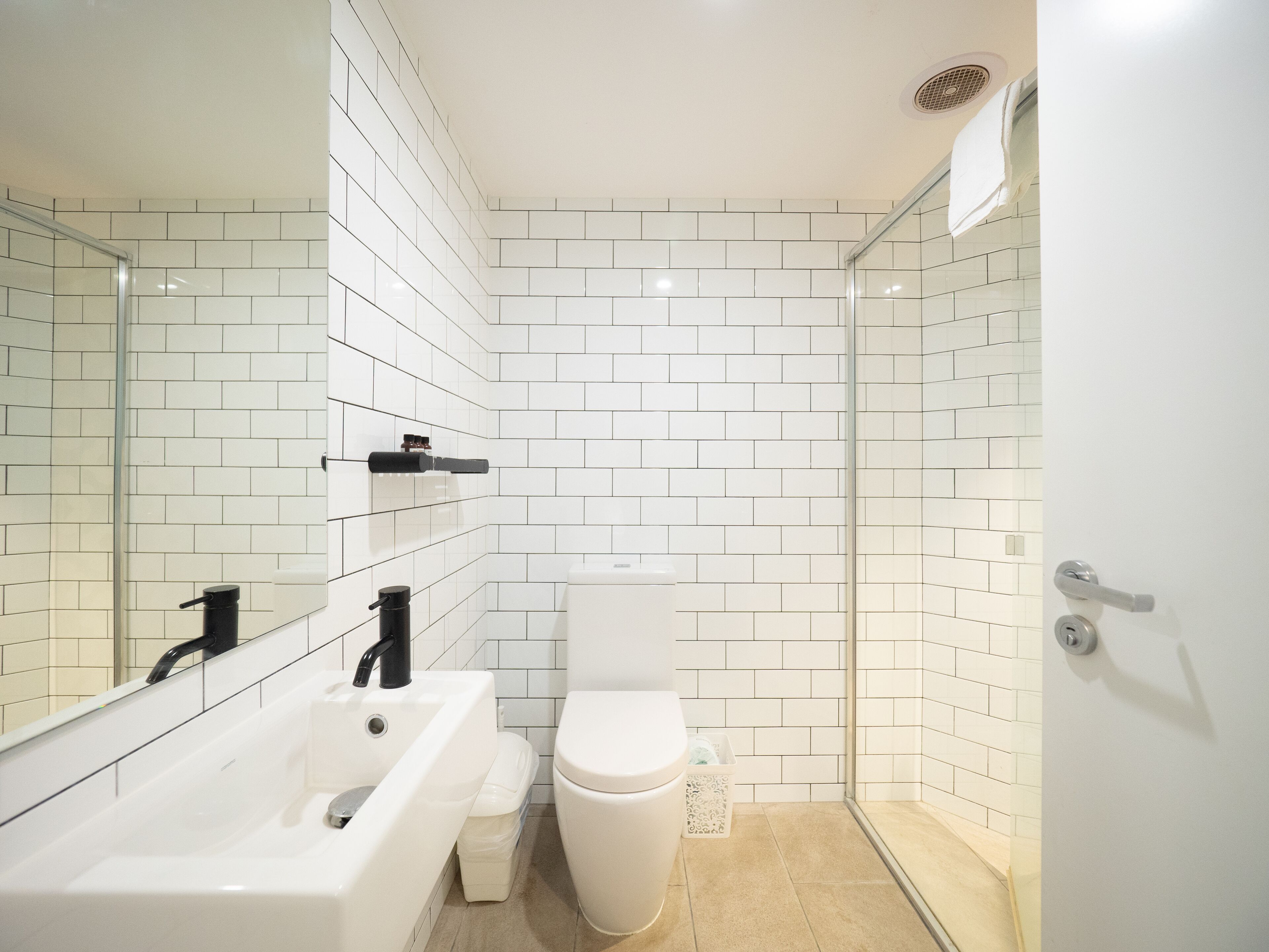 Une salle de bain moderne avec des murs recouverts de carreaux blancs, une baignoire, des toilettes et une douche à parois de verre.