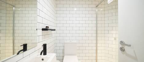 A modern bathroom with white tiled walls, a bathtub, a toilet, and a glass shower enclosure.