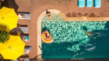 An aerial view of a swimming pool with lounge chairs and umbrellas, surrounded by a brick patio.