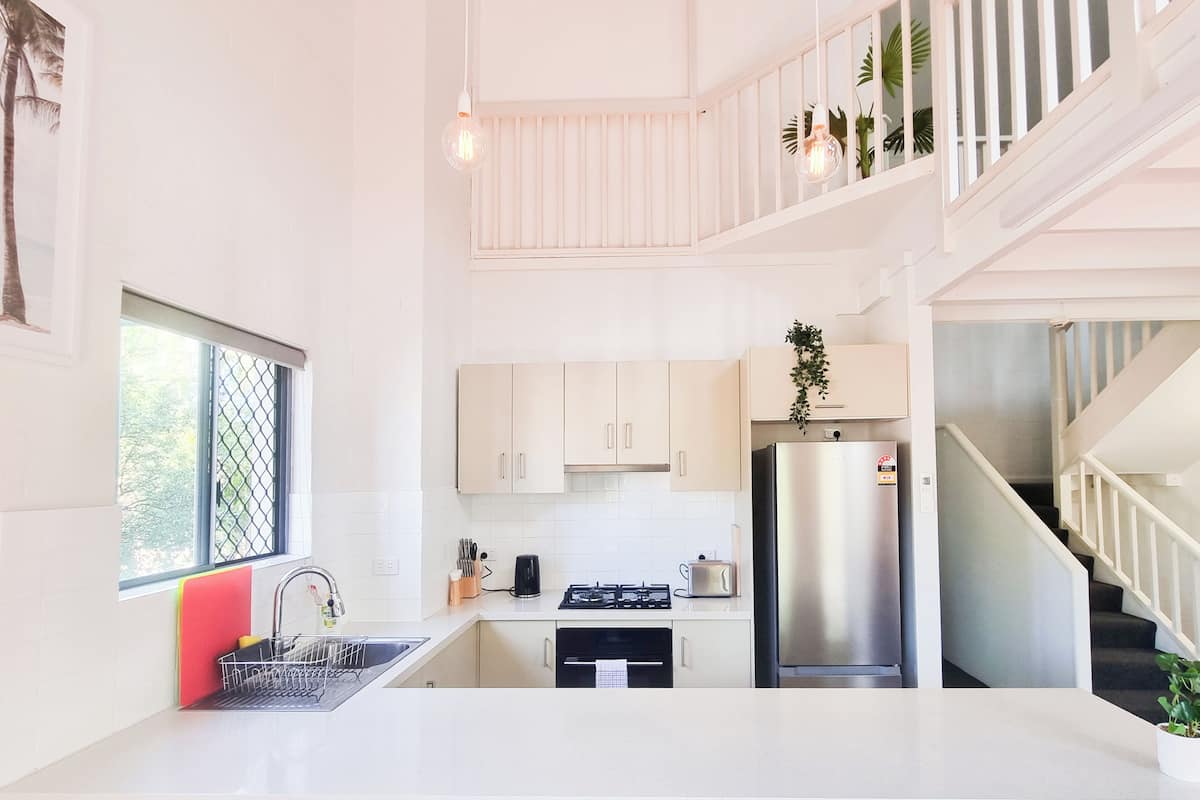 A modern kitchen with white cabinets, a stainless steel refrigerator, and a window with a view of greenery.