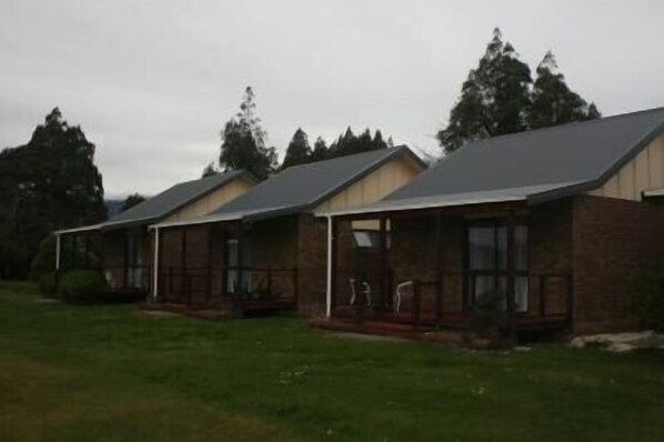 A row of single-story cabins with attached porches, surrounded by a grassy area and tall trees.