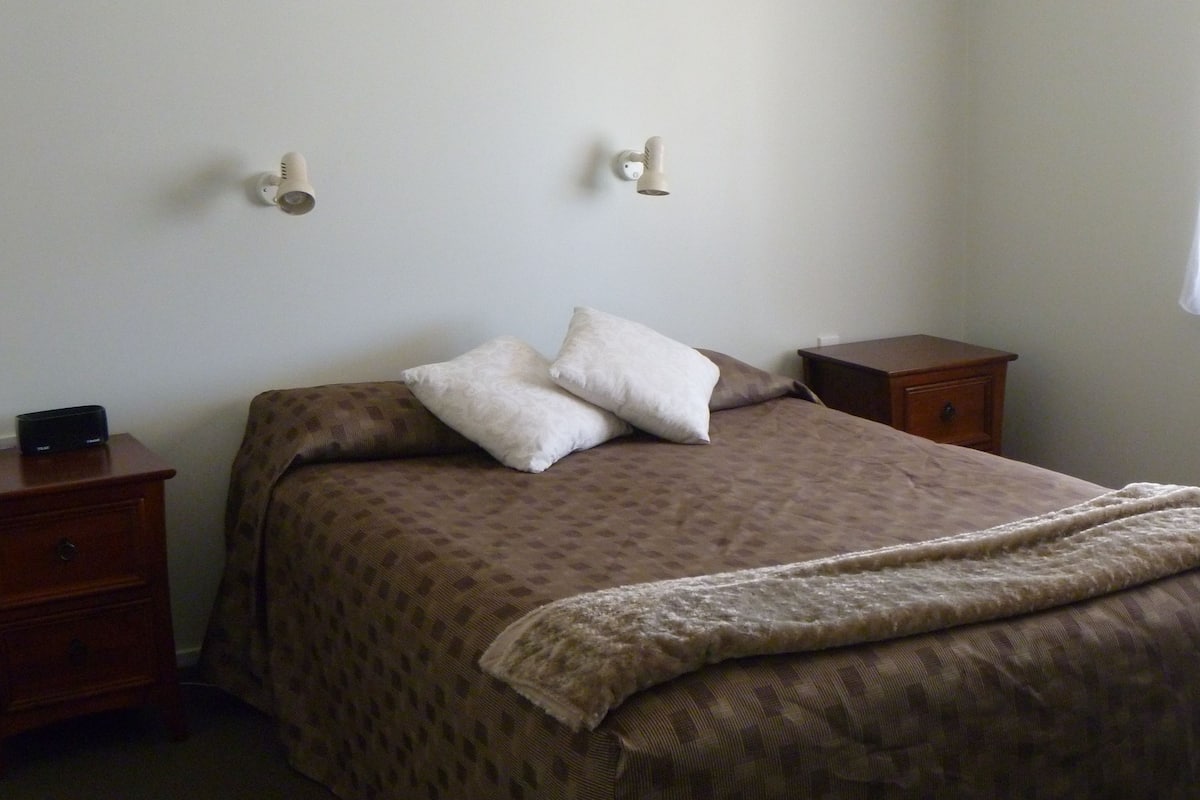 A bedroom with a bed, two bedside tables, a window, and a wall-mounted light fixture.