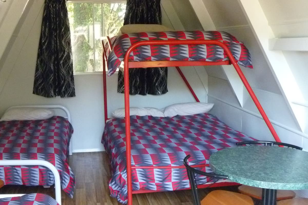 A small, triangular tent-style room with two bunk beds, a small table, and a window with curtains.