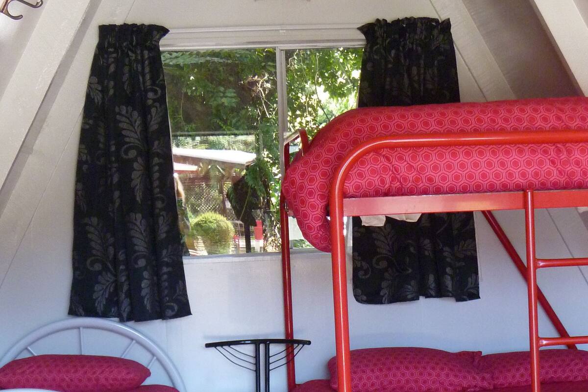 A dormitory room with bunk beds, a single bed, a chair, and a window with curtains.