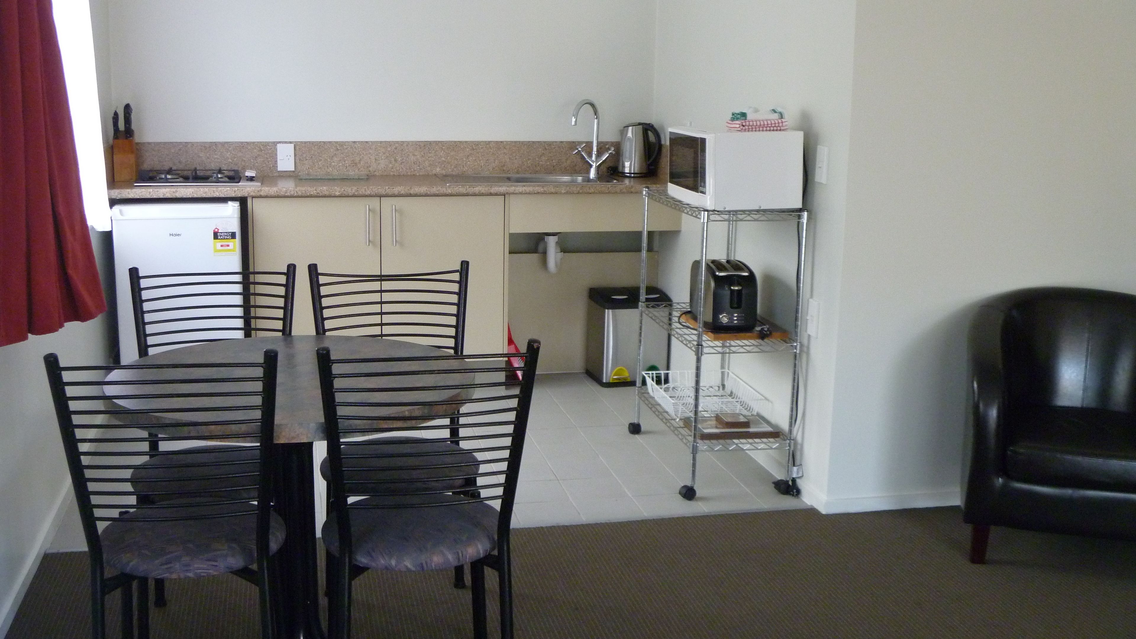 Una cocina compacta con una mesa de comedor, sillas, microondas, tostadora y un refrigerador pequeño.