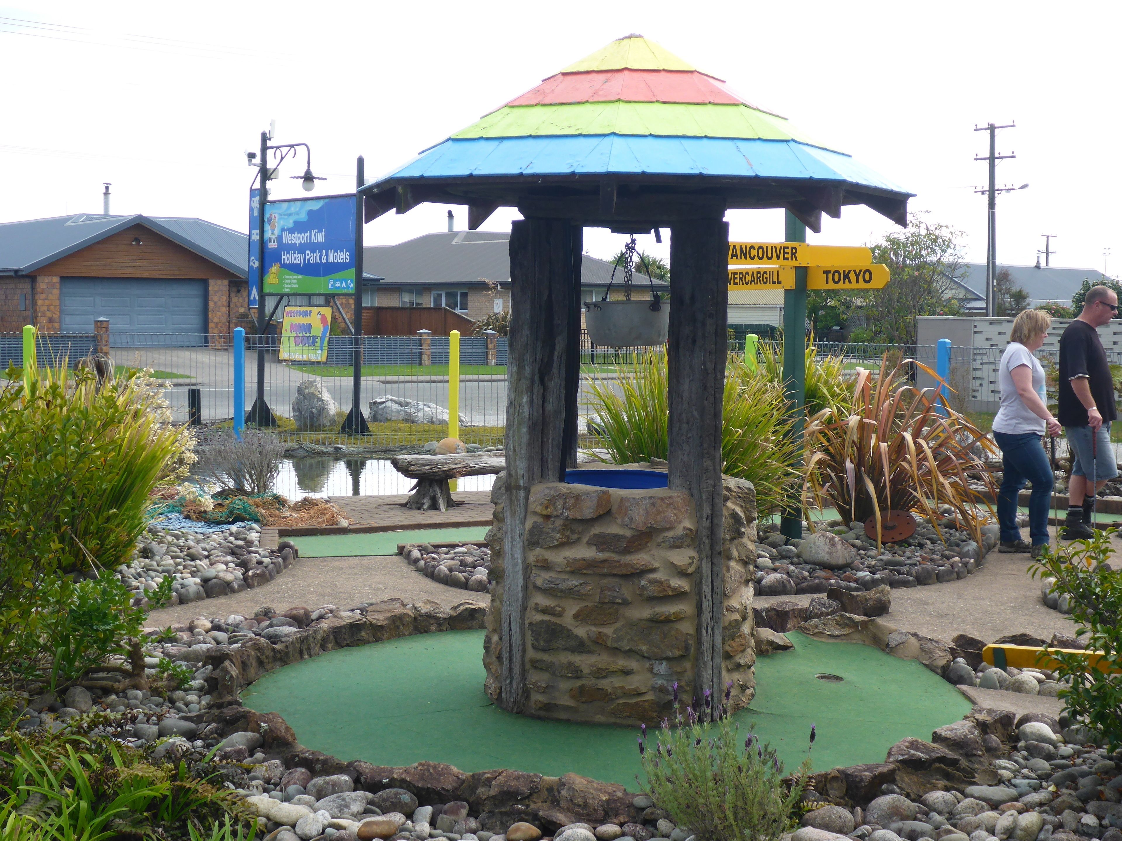 Un camp de mini-golf amb una estructura de para-sol de colors, envoltat de roques i plantes.
