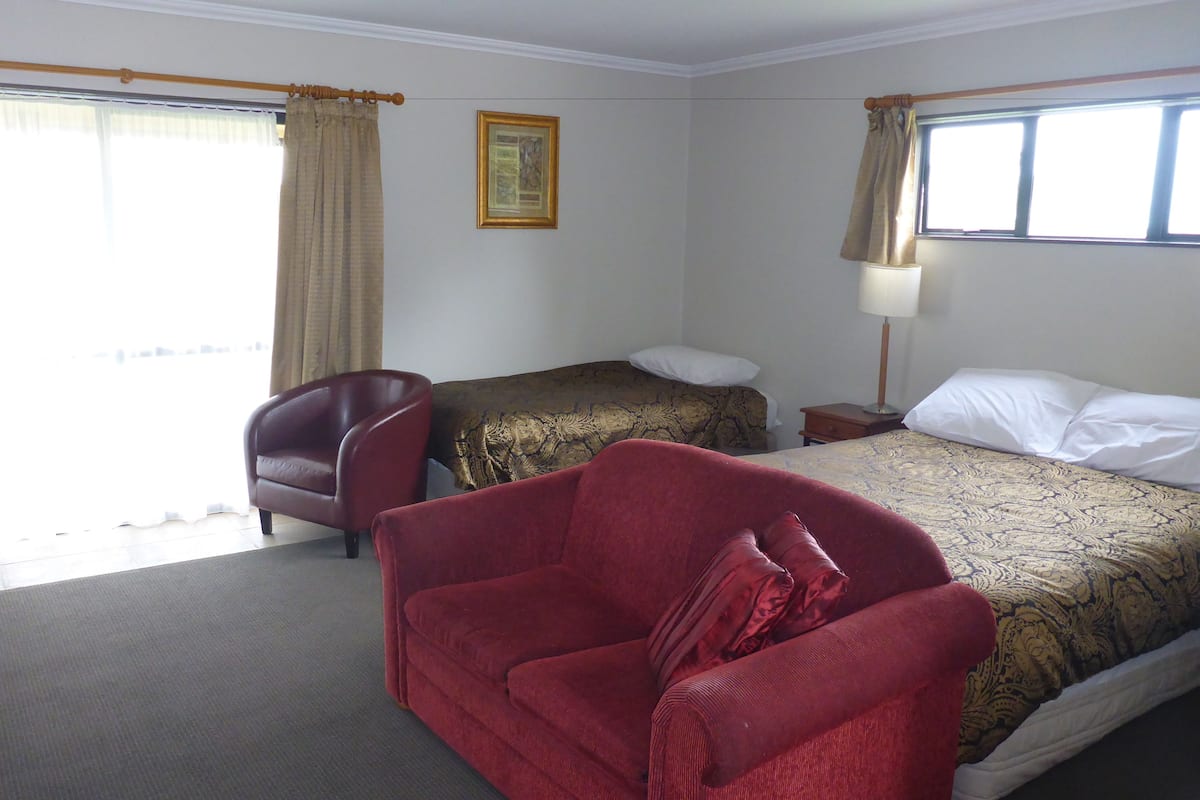 A hotel room with a bed, a red armchair, a small table, and a nightstand.
