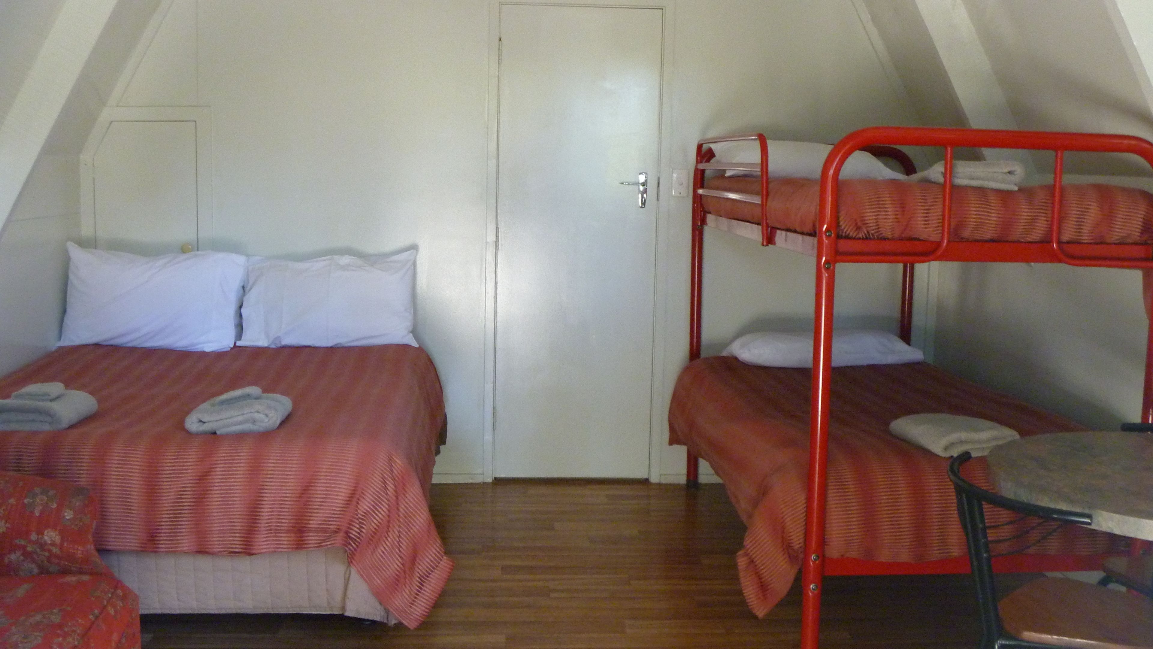 Een studentenkamer met twee bedden, een houten vloer en een deur.