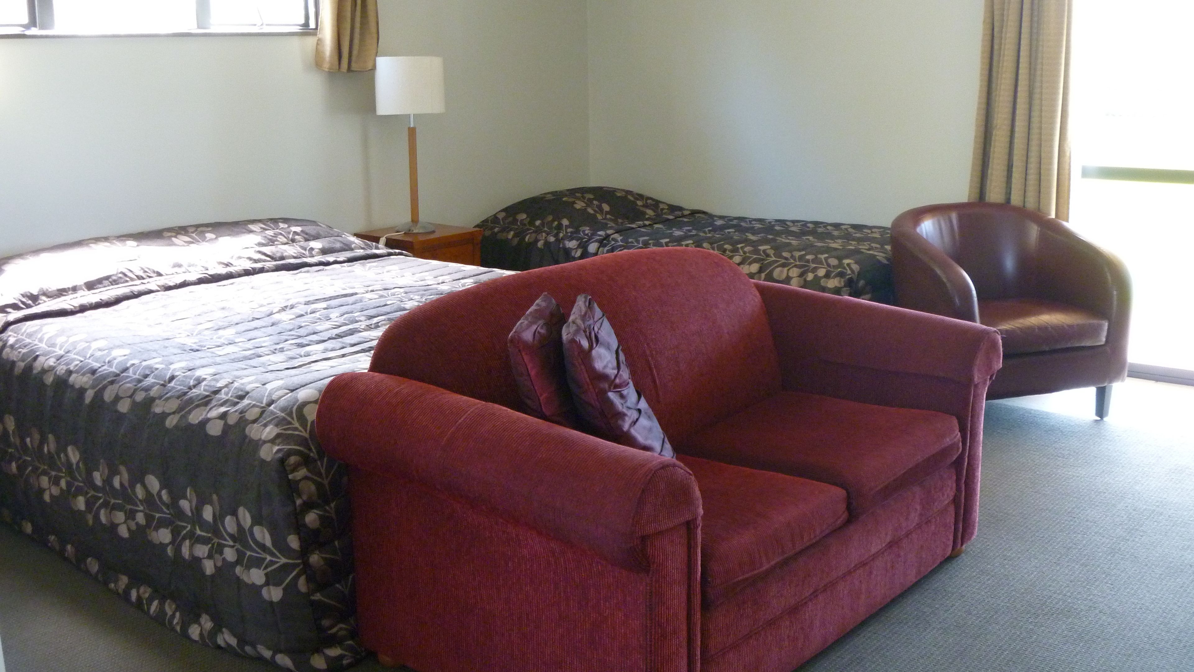Una habitación de hotel con una cama grande, un sillón rojo, un sofá más pequeño y una lámpara.